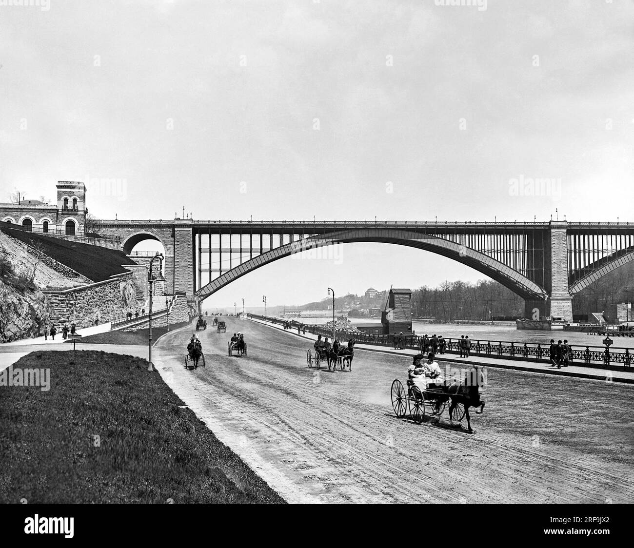 New York, New York:  c. 1901 A view of the Harlem River Speedway with the Washington Bridge in the background. It was initially open only to carriages and sulkies so the wealthy could parade their trotting horses down the 2.5 mile dirt roadway. Pedestrians, horseback riders, and cyclists were prohibited. Stock Photo