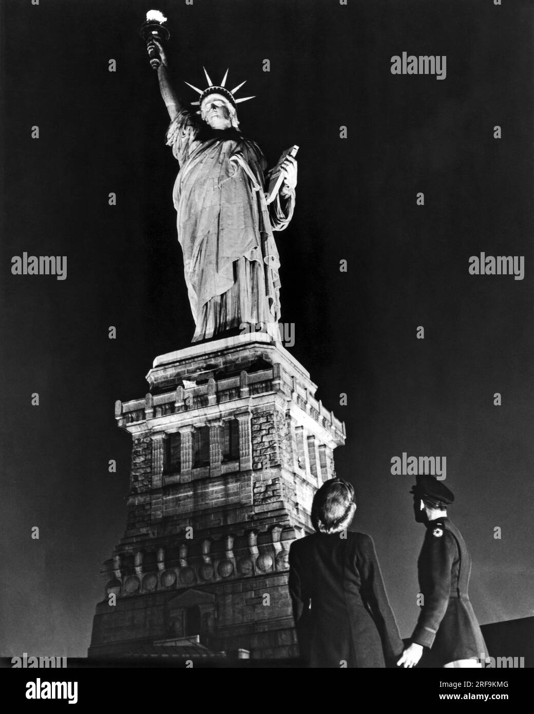 New York, New York:  May 8, 1945 A soldier and his companion gaze up on V-E Day at the Statue of Liberty after it was illuminated, except for a brief period on D-Day, for the first time since the Pearl Harbor attack. Stock Photo