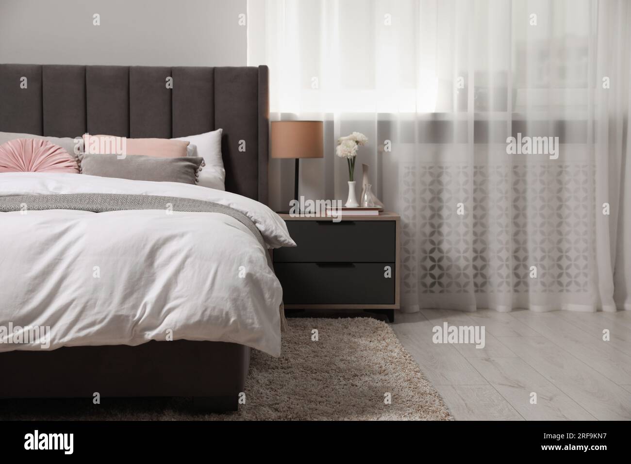 Comfortable bed with cushions, lamp and different decor on bedside table in room. Stylish interior Stock Photo