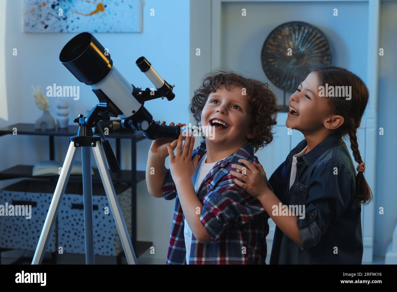 Cute little children using telescope to look at stars in room Stock