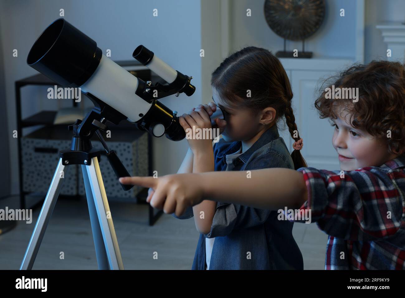 Cute little children using telescope to look at stars in room Stock