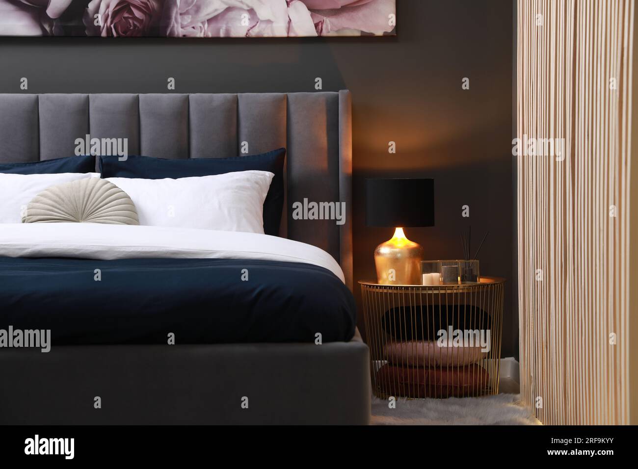 Comfortable bed with cushions, lamp and different decor on bedside table in room. Stylish interior Stock Photo