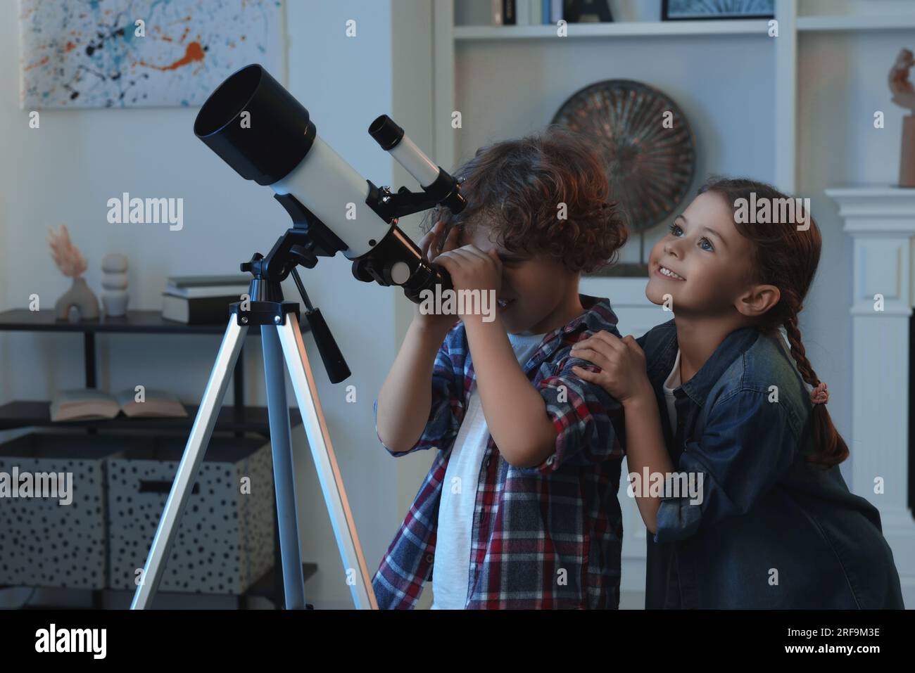 Cute little children using telescope to look at stars in room Stock