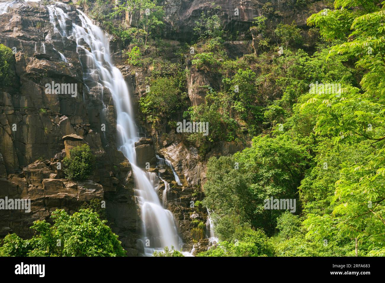 Silky milky smooth Sita waterfall flowing over green rocky hills at ...