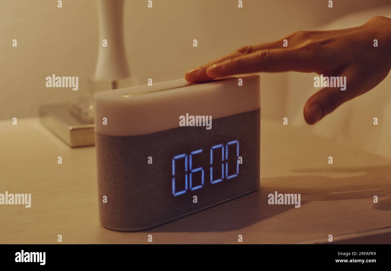 Young woman’s hand turning off digital alarm clock on nightstand in the bedroom at home. Stock Photo
