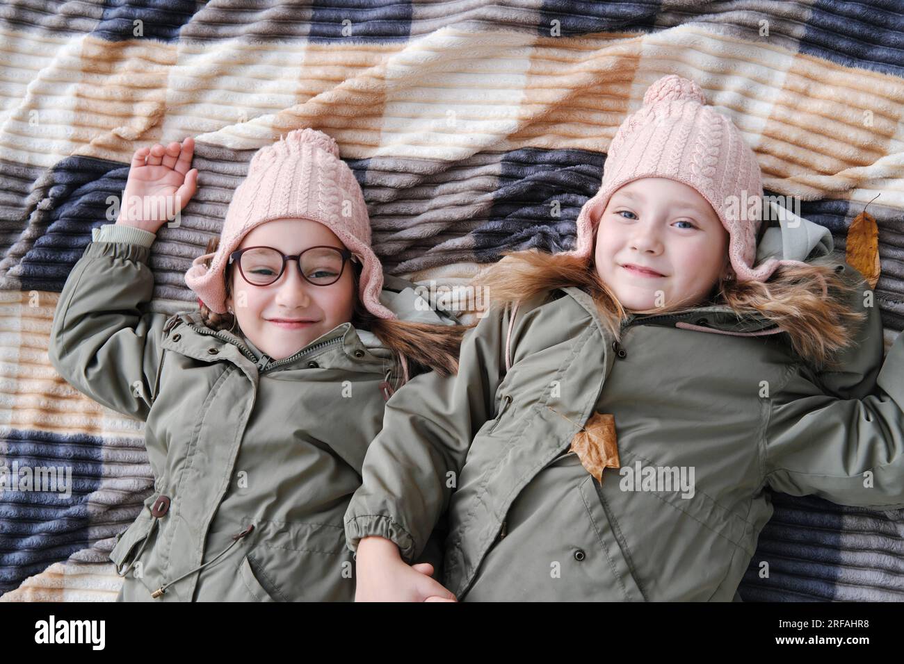 Two happy twin sisters lie on a blanket in an autumn park. The girls ...