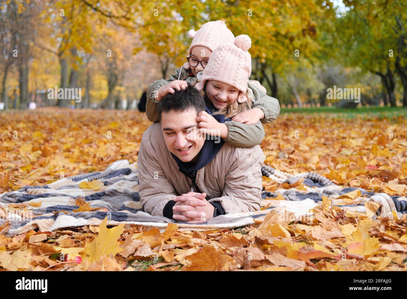 Family day in autumn park. Father with daughters lies on a blanket and plays. Daughters tickle father. Horizontal photo Stock Photo