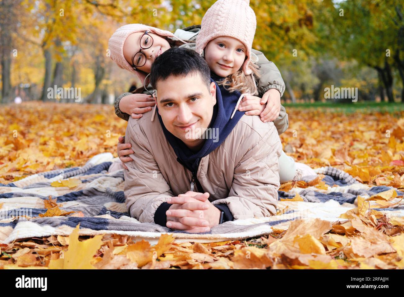 Family day in autumn park. The twin girls lie on their father's back. Father and sisters smiling and looking at the camera. Horizontal photo Stock Photo