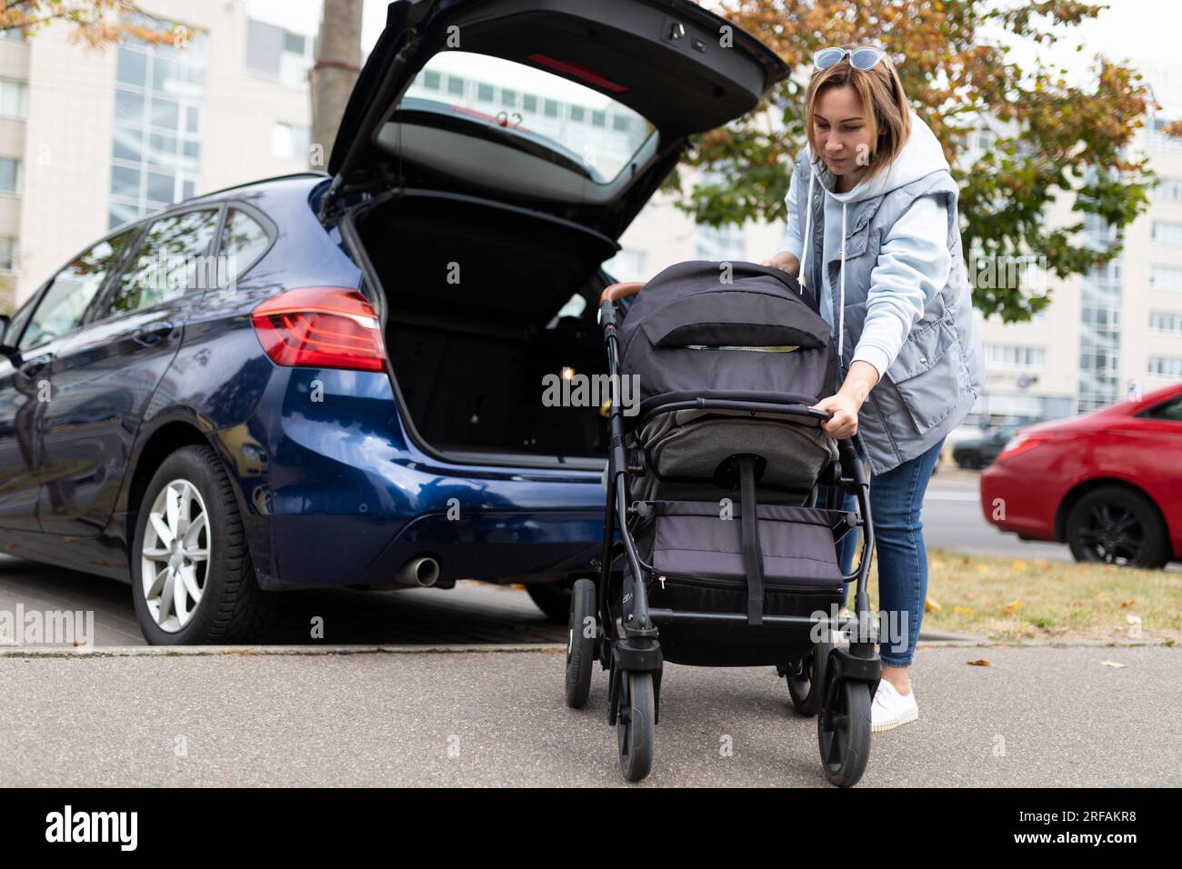 mom driver puts the baby stroller in the luggage compartment of the car