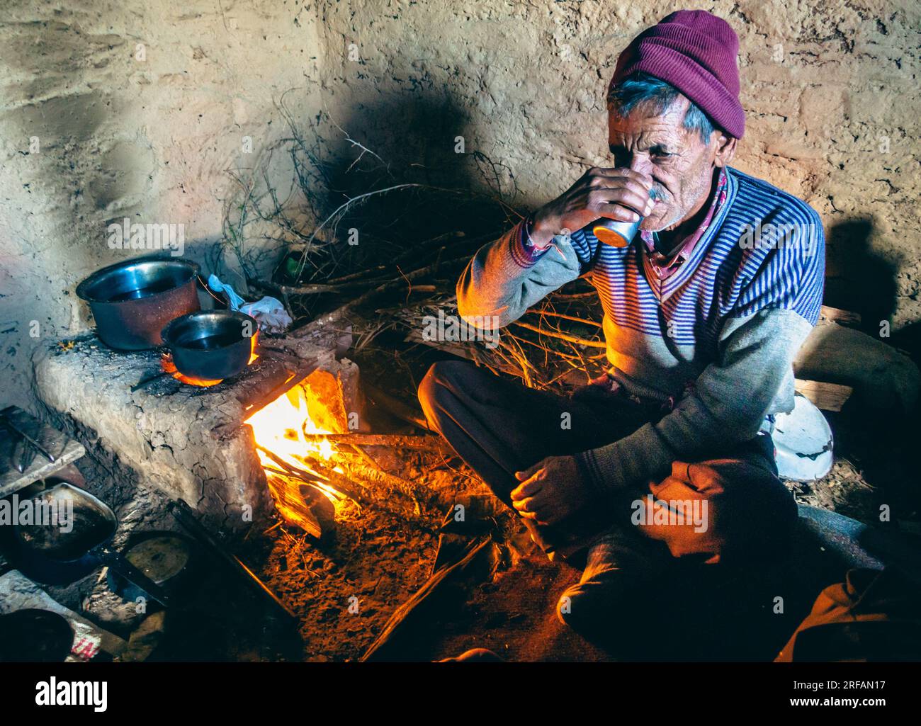 Oct.14th 2022 Uttarakhand, India. Elderly native enjoying tea in traditional mud house with clay stove in Garhwal, Himalayas. Rich cultural heritage c Stock Photo