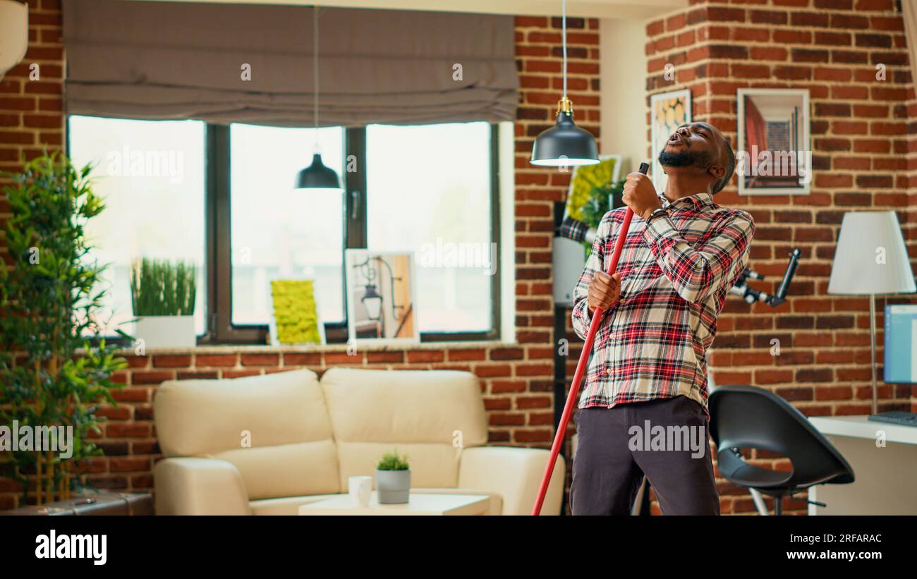 Cheerful man mopping apartment floors and listening to music, acting