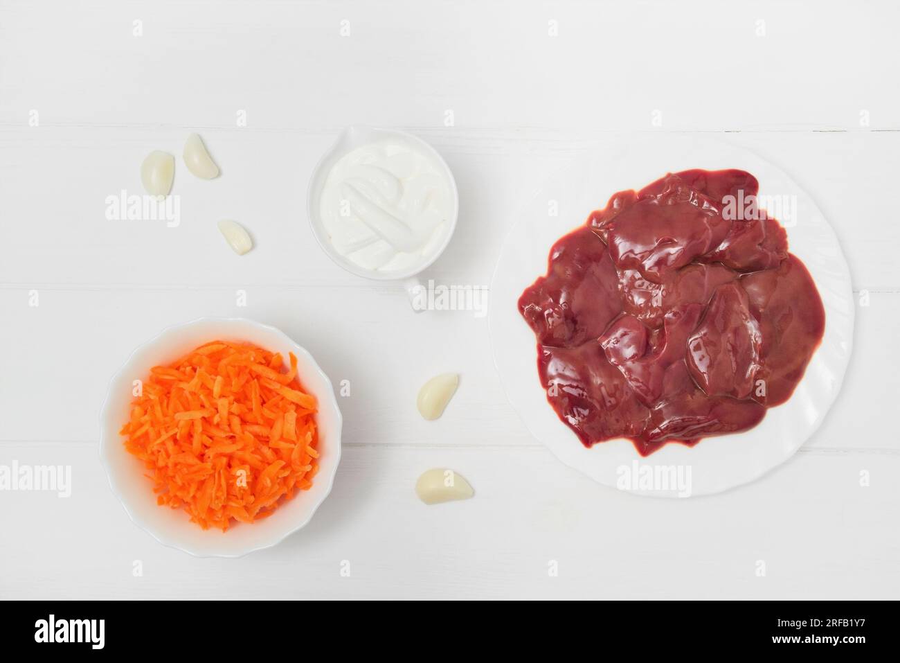 Fresh raw chicken liver and grated carrots in a plate and garlic cloves, Sour cream gravy boat