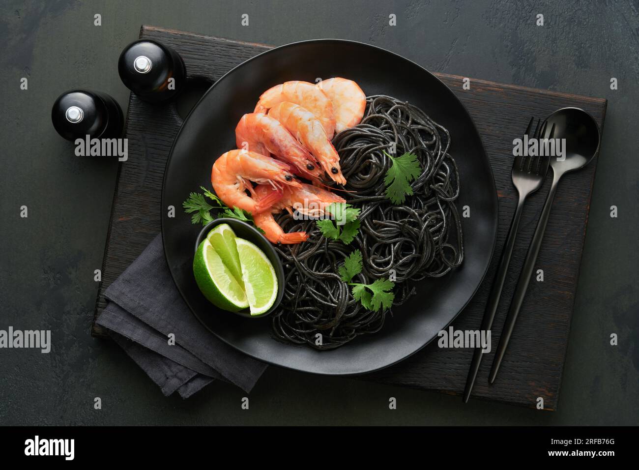 Black spaghetti pasta shrimp on black plate on dark concrete table background. Squid ink pasta with prawns. Pasta seafood. Top view on black stone tab Stock Photo