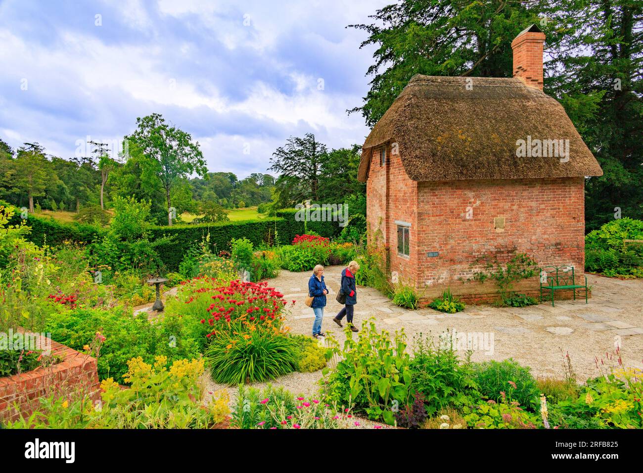 A small red brick cottage with thatched roof surrounded by colourful borders in the Cottage Garden at 'The Newt in Somerset', nr Bruton, England, UK Stock Photo