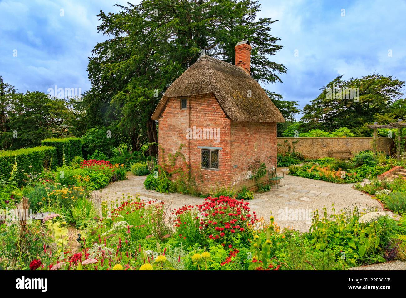A small red brick cottage with thatched roof surrounded by colourful borders in the Cottage Garden at 'The Newt in Somerset', nr Bruton, England, UK Stock Photo