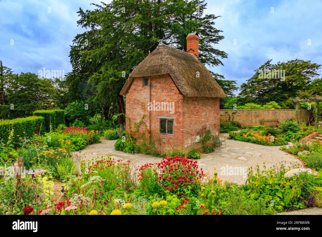 A small red brick cottage with thatched roof surrounded by colourful ...