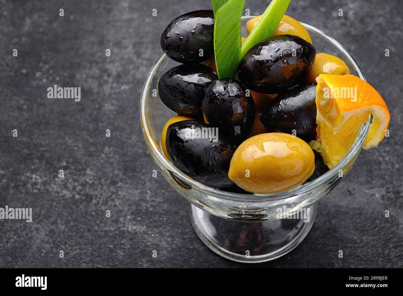 Large olives, green and black in a glass dish, on dark concrete. Close up Stock Photo