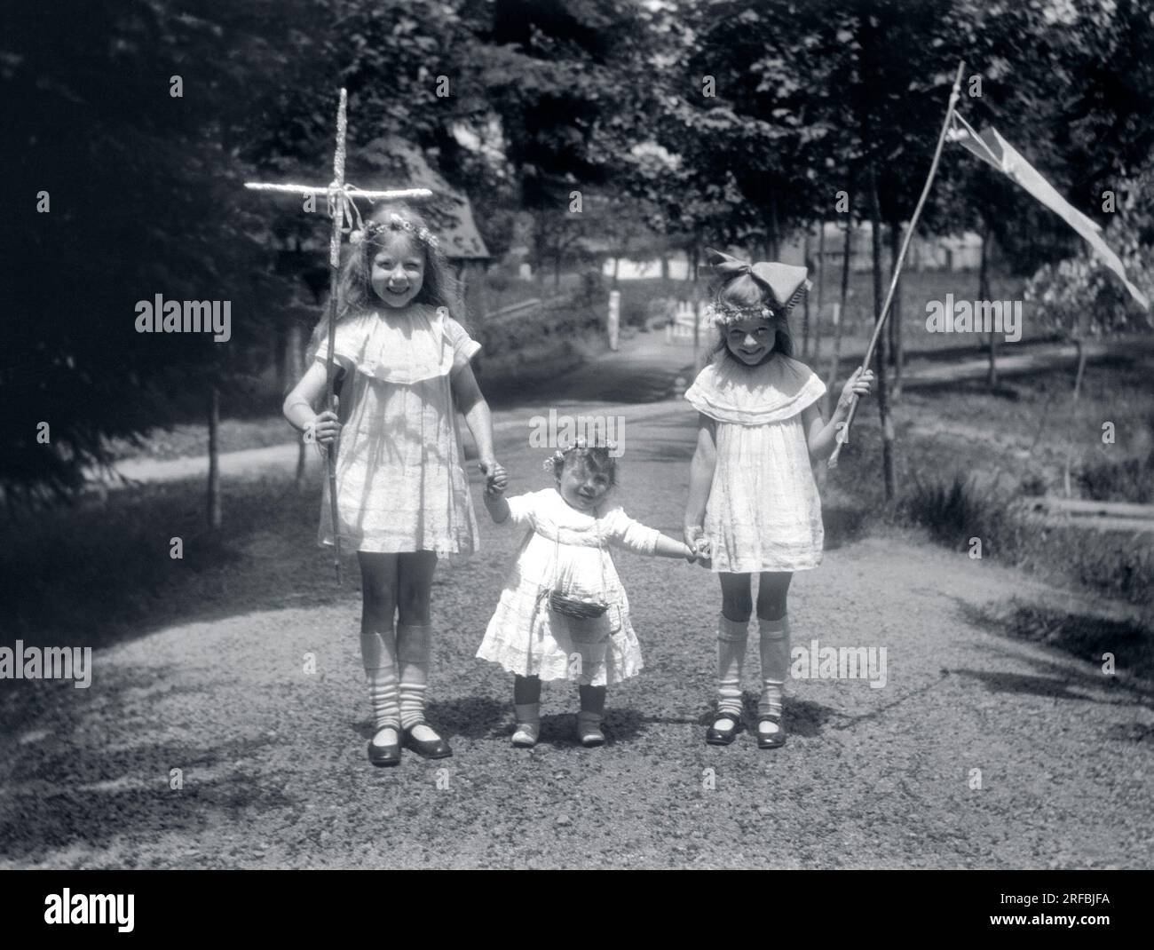 Trois petites filles, en robes de dentelle, portant croix, panier et fanion pour une procession. Bretagne (France), photographie 1921-1922. Stock Photo