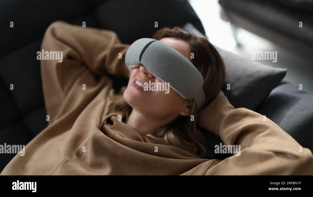 Tired woman uses massager while lying on sofa Stock Photo