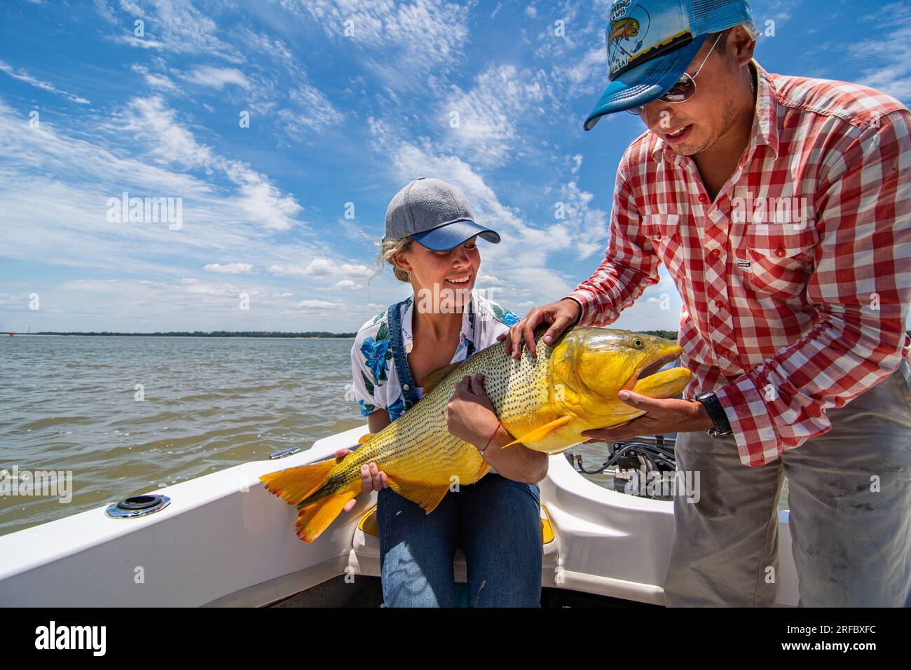 Grown white man and young woman holding a big specimen of golden dorado (Salminus Brasiliensis) during a fishing day. Stock Photo
