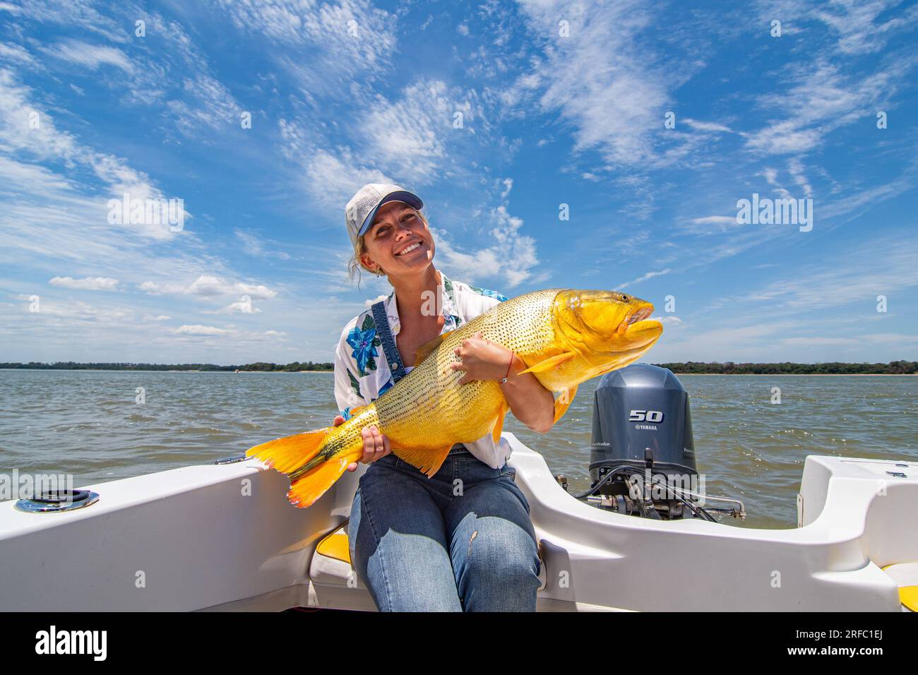 Young white woman holding a big specimen of golden dorado (Salminus Brasiliensis) during a fishing day. Stock Photo