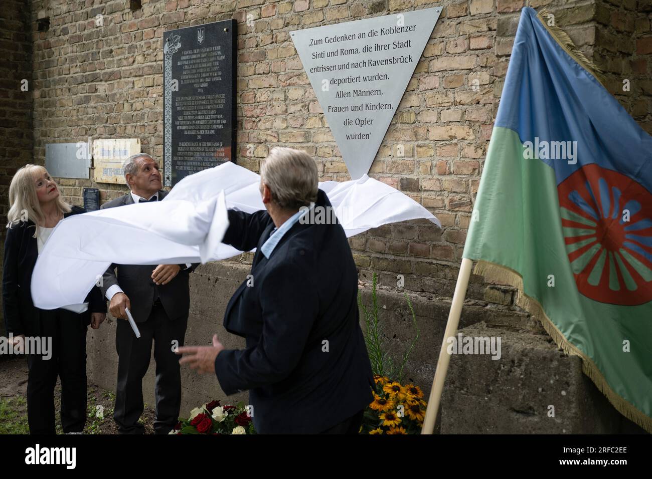 02 August 2023, Brandenburg, Fürstenberg/Havel: Margit Theis-Scholz (l), Head of Education & Culture of the City of Koblenz, and Heinrich Django Reinhardt (2nd from left) unveil the memorial plaque together. At the Ravensbrück Memorial, there is a new memorial plaque for Sinti and Roma who were deported to the concentration camp during the Nazi era. Photo: Hannes P. Albert/dpa Stock Photo