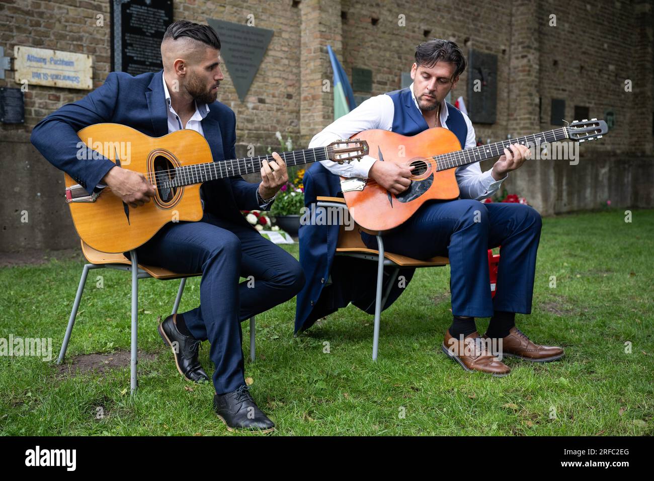 02 August 2023, Brandenburg, Fürstenberg/Havel: Marlon Reinhardt (from left) and Taylor Swing (from right) play guitar at the event for a new memorial plaque for Sinti and Roma in Ravensbrück . There is a new memorial plaque at the Ravensbrück Memorial for Sinti and Roma who were deported to the concentration camp during the Nazi era. Photo: Hannes P. Albert/dpa Stock Photo