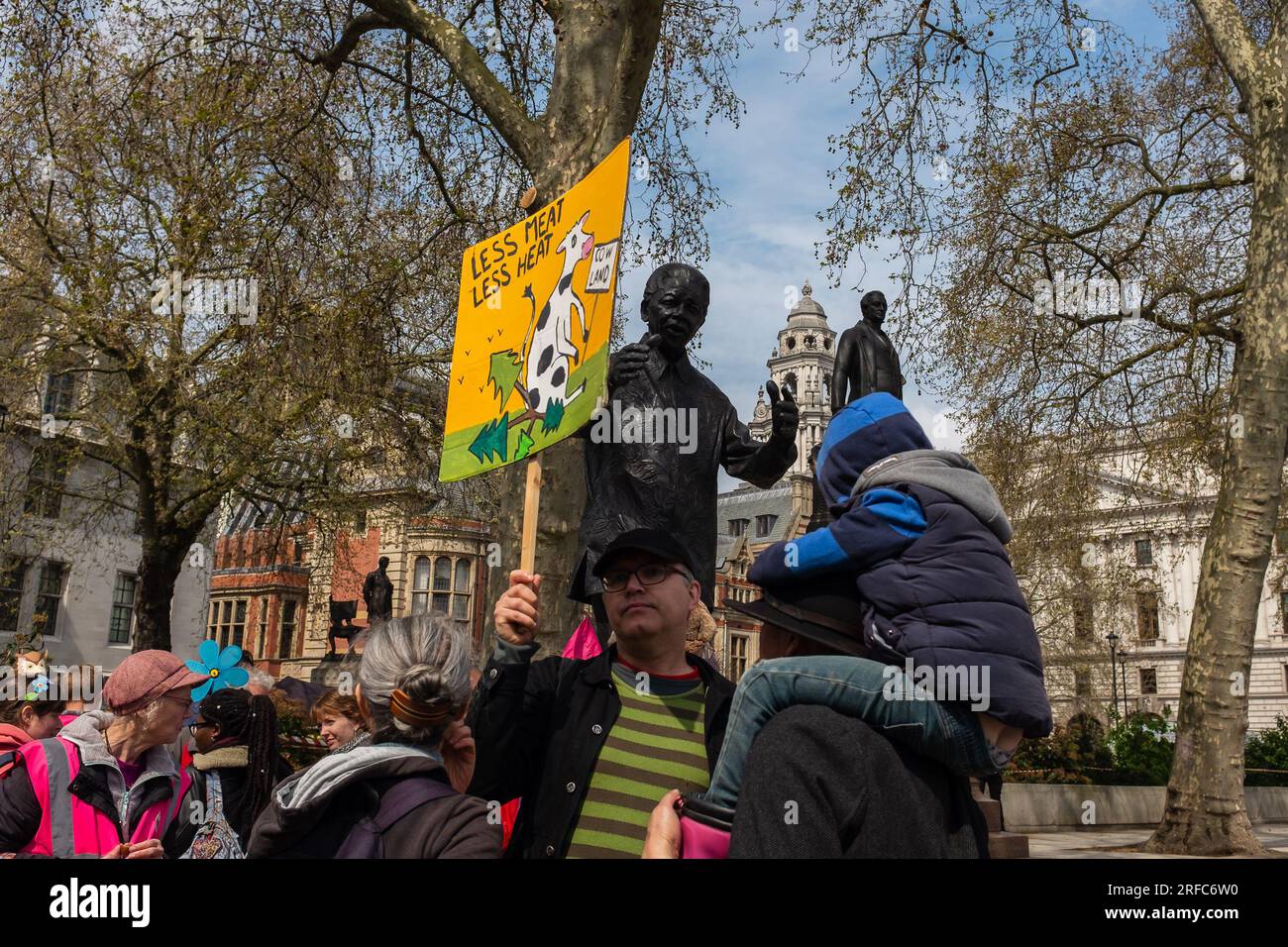 London, UK, 2023. On Earth Day, a climate activist is holding up a sign that reads, Less Meat Less Heat, in front of Nelson Mandela's statue Stock Photo