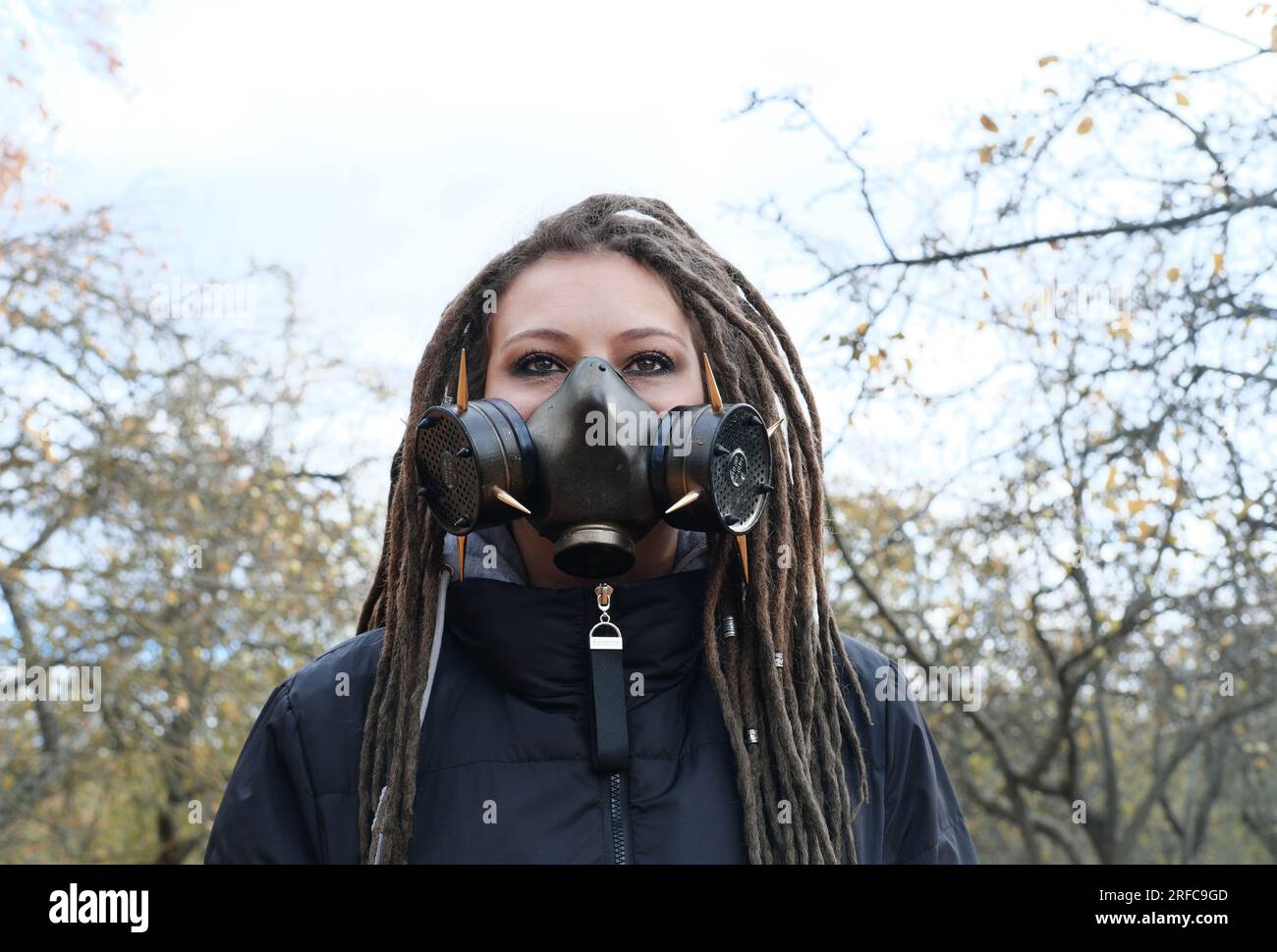 Portrait of a Woman in a black jacket with dreadlocks and a gas mask with spikes. Woman posing in autumn park. Horizontal photo Stock Photo