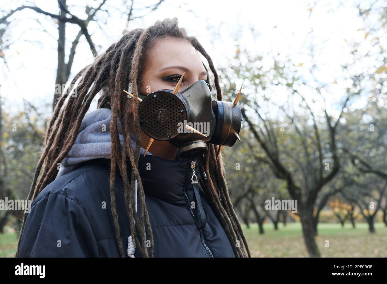 Portrait of a Woman in a black jacket with dreadlocks and a gas mask with spikes. Woman posing in autumn park. Horizontal photo Stock Photo