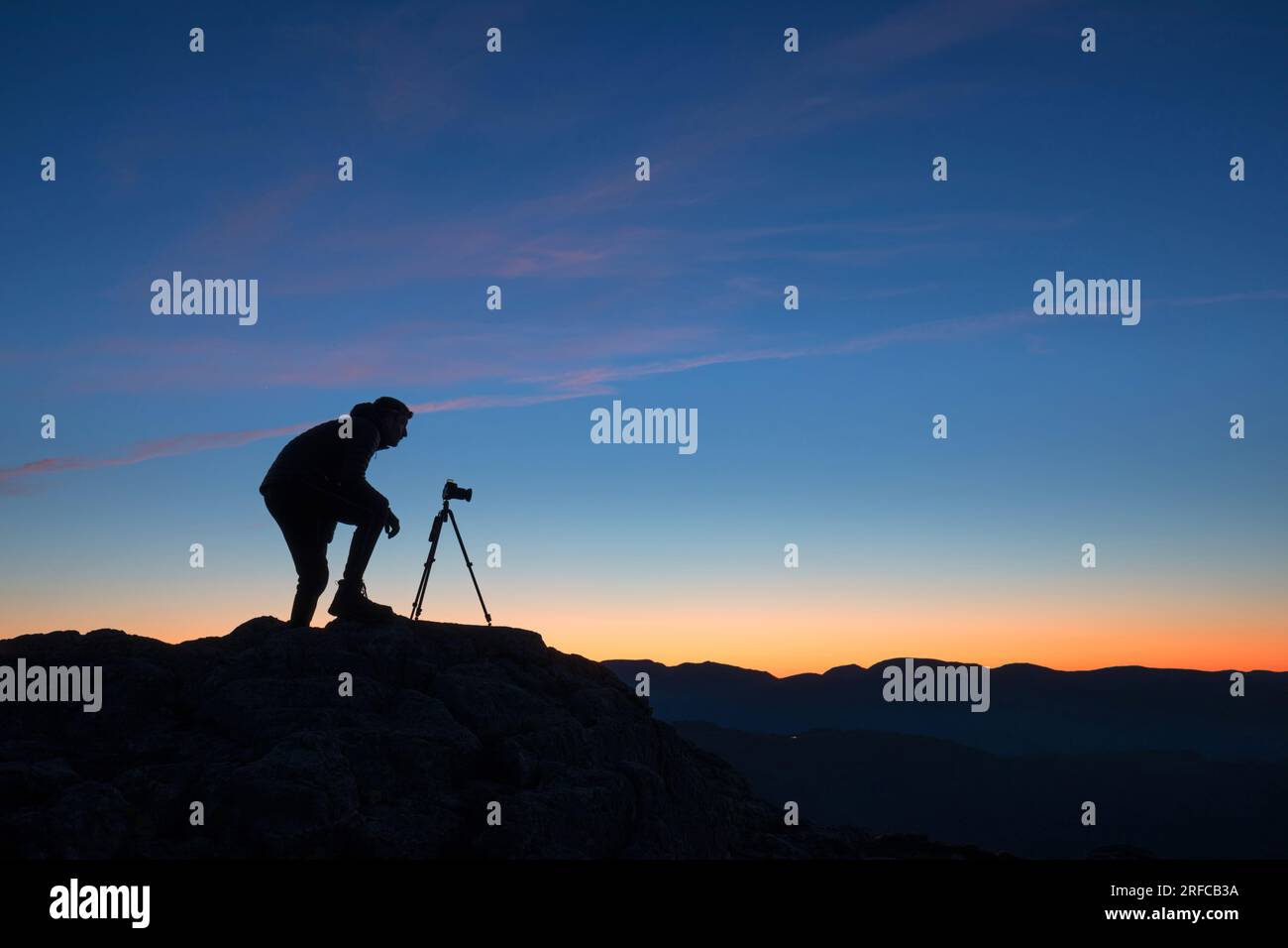 Photographer standing by tripod on top of mountain at sunrise, lake District UK Stock Photo