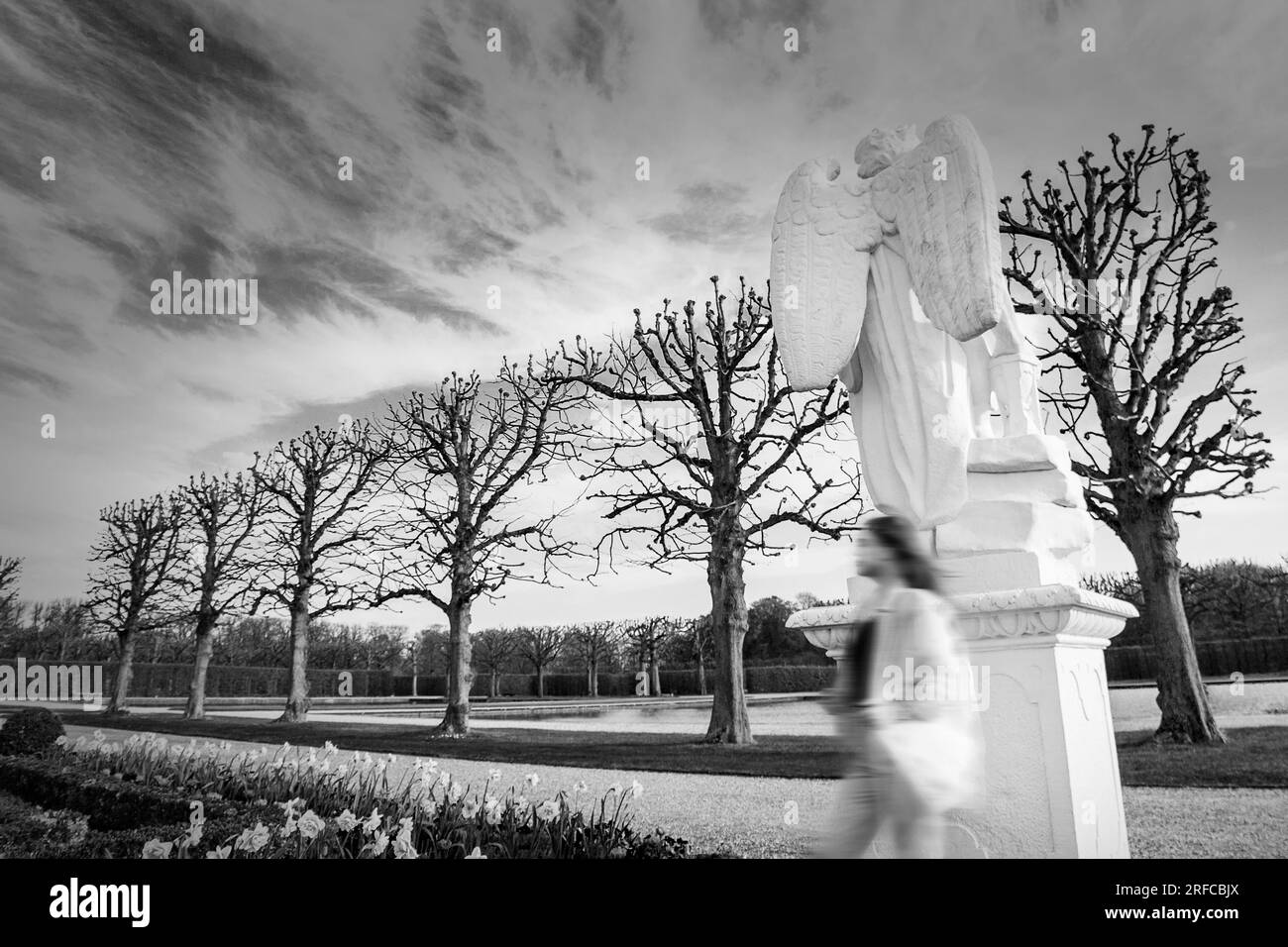 Ghost in the park. Black and white photography. A defocused person against the background of a moody sky and a sculpture of an angel. Stock Photo
