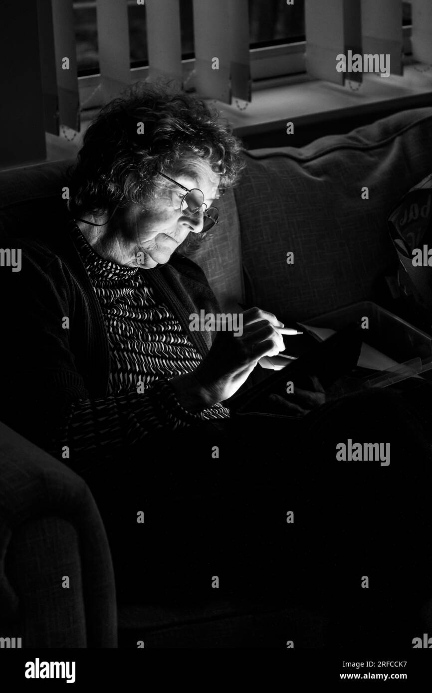 Female artist painting on an iPad tablet during the evening in subdued lighting monochrome image Stock Photo