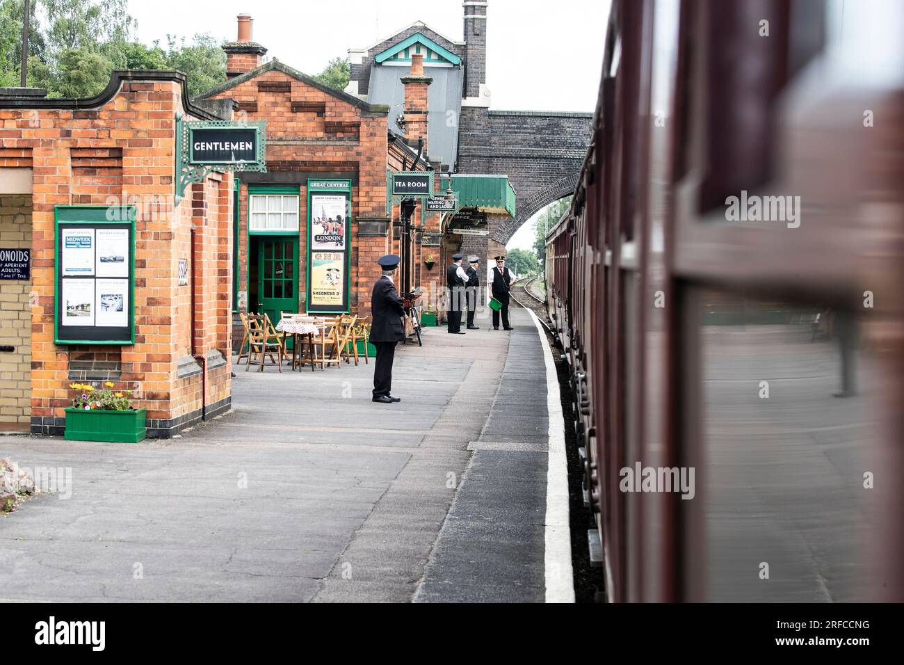 Station staff in period uniform on the platform at Rothley railway station as the heritage steam train passes through on the way to Leicester North Stock Photo