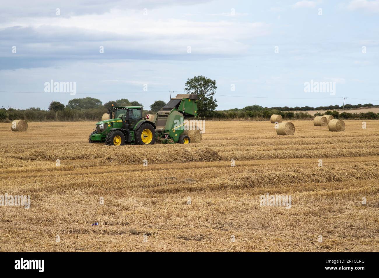 John Deere farm tractor and baling machine baling hay in a wheat field in East Yorkshire Stock Photo