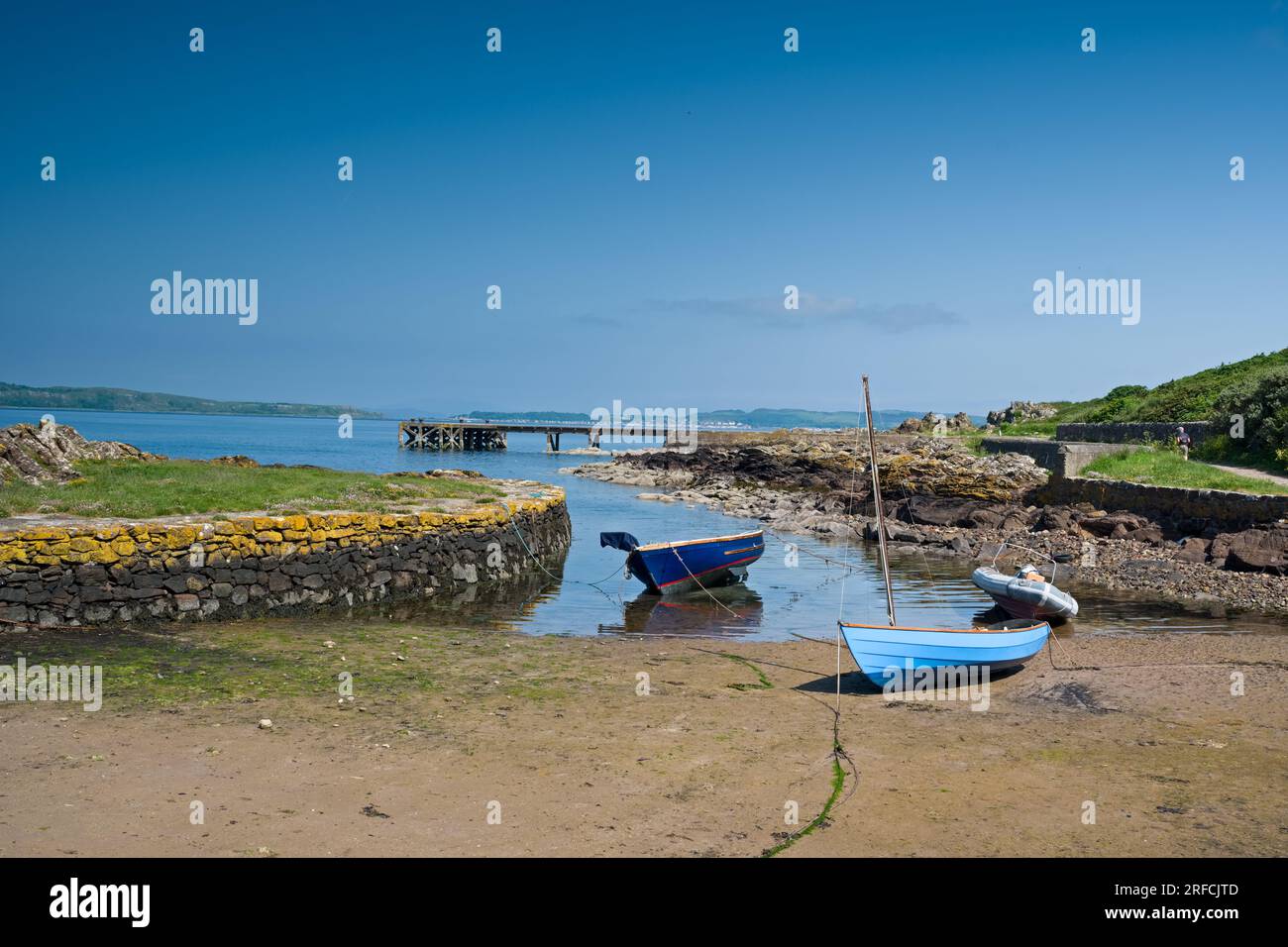 Looking over the rocky harbour  to the old jetty and some small boats at Portencross in Seamill West Kilbride on a bright summers day in June with blu Stock Photo
