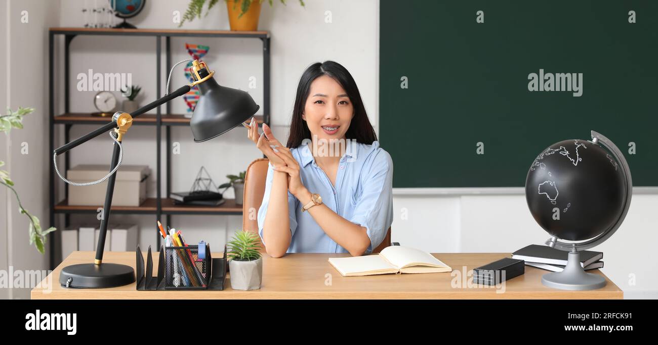 Female Asian teacher sitting at table in classroom Stock Photo - Alamy