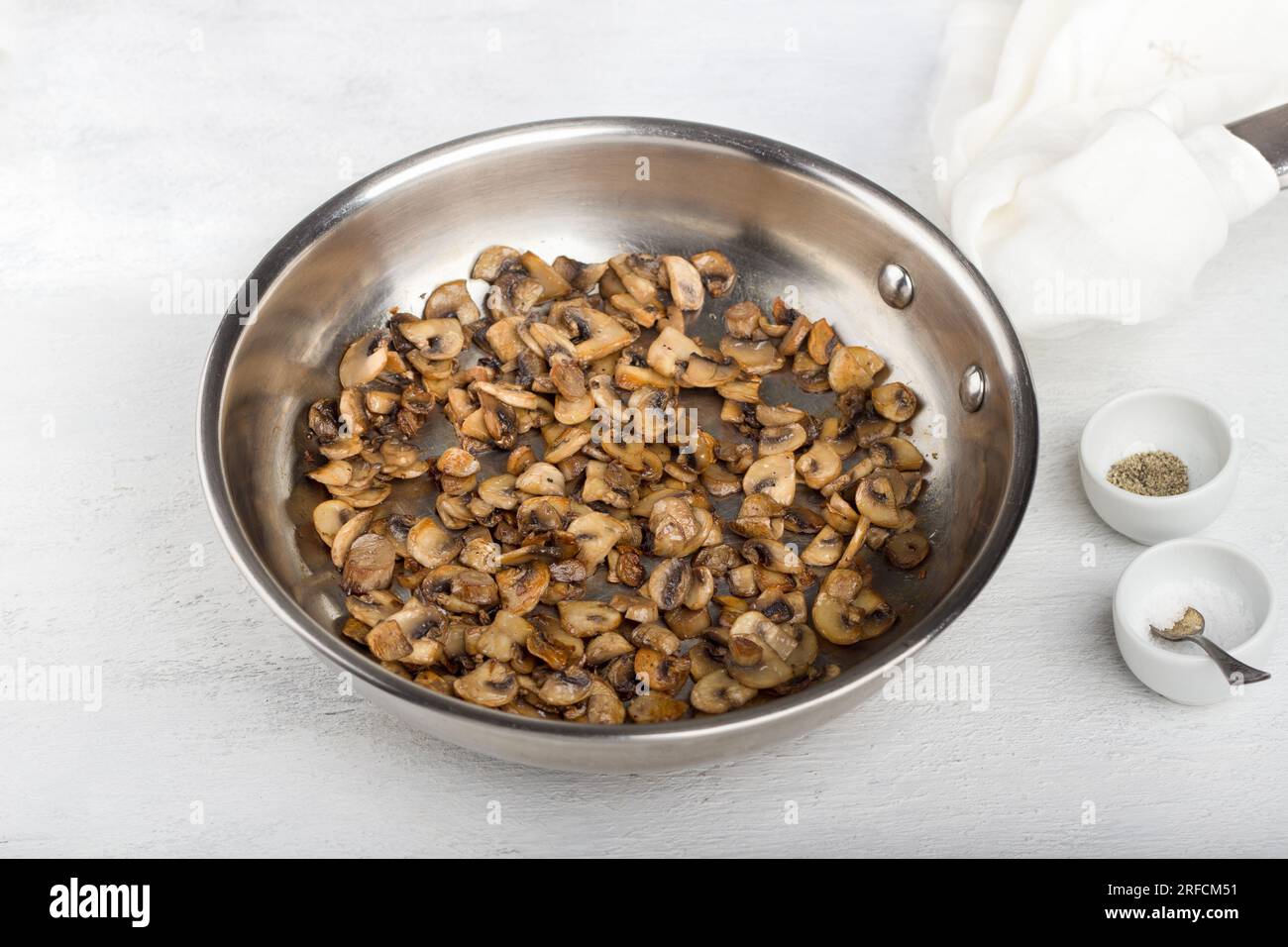 Frying pan with fried champignon mushrooms with spices on a light gray background. Stage of cooking a delicious vegetarian dish. Stock Photo