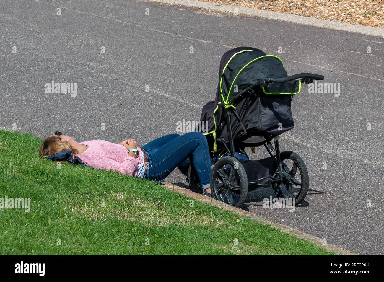 young mother with pushchair taking a rest. young mum sleeping next to pushchair on a warm summers day. mum taking a break from childcare having a nap. Stock Photo