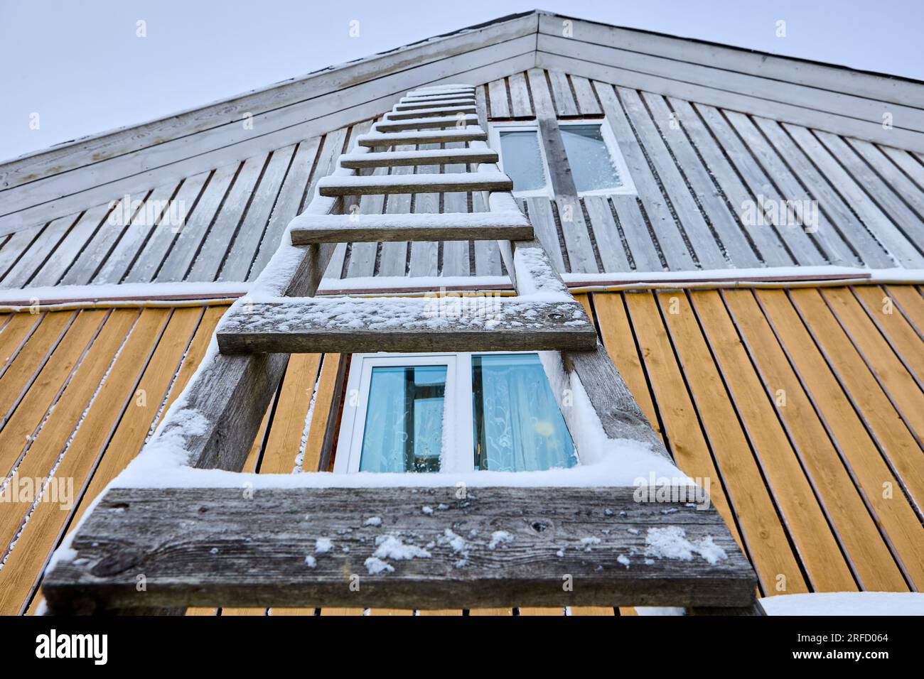 Wooden lean to ladder with rungs is leaning against the wall of wooden rural house in winter. Stock Photo
