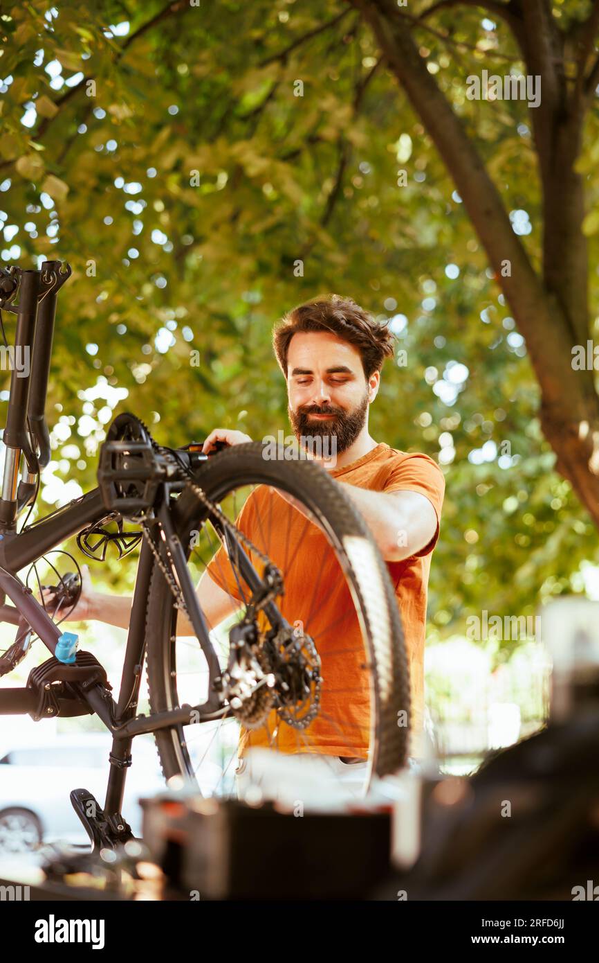 Enthusiastic male cyclist upkeeping and servicing bicycle in home yard. Dedicated sporty caucasian man inspecting and performing bike maintenance for outdoor leisure cycling. Stock Photo