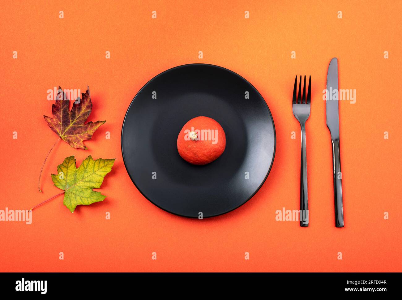 Autumn table place setting with black plate with pumpkin on orange background. Thanksgiving, halloween decoration. Top view, flat lay. Stock Photo