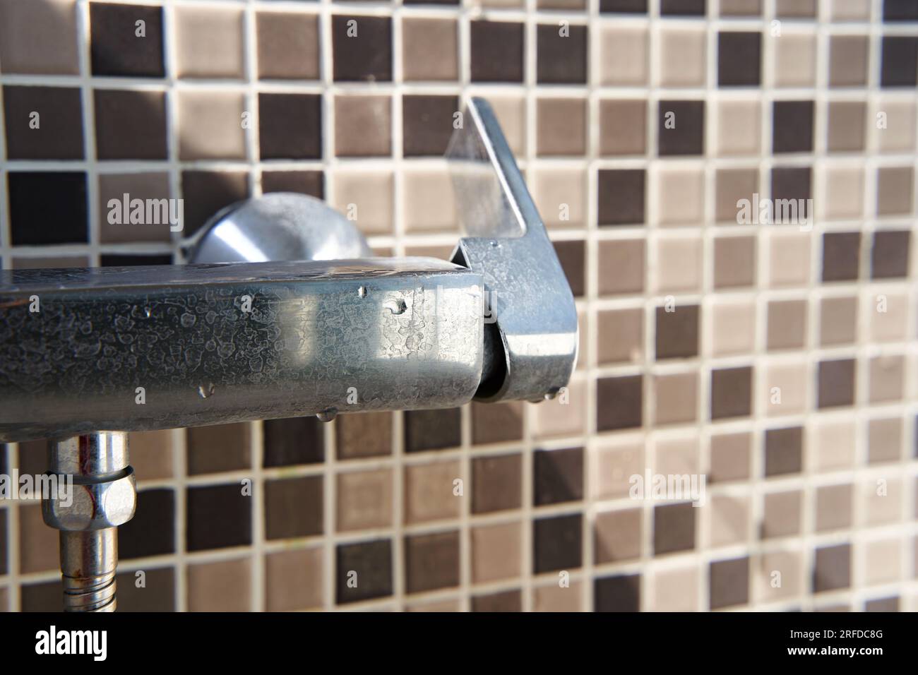 Limescale on the dirty faucet switch in the shower room. Brown tiles on