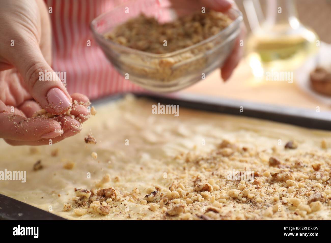 Making delicious baklava. Woman adding chopped nuts to dough, closeup Stock Photo