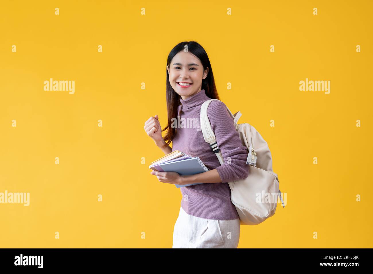 A cheerful young Asian female college student with a backpack holding ...