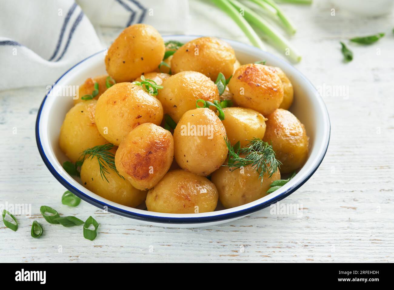 Boiled new or young potatoes with butter, fresh dill and onions in white bowl on white old rustic wooden background. Tasty new boiled potatoes. Top vi Stock Photo