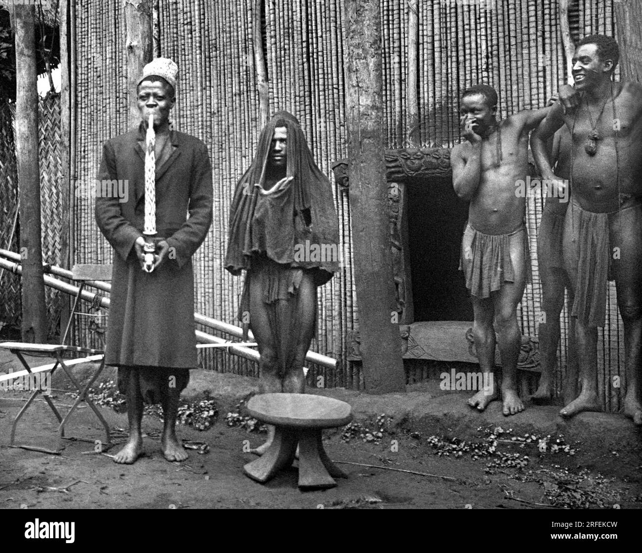Un chef et son 'djoudjou' a demi voile,  observes par deux curieux, a Bana ( Cameroun). Photographie des missions du Sacre Coeur de Jesus, debut XXeme siecle. Stock Photo