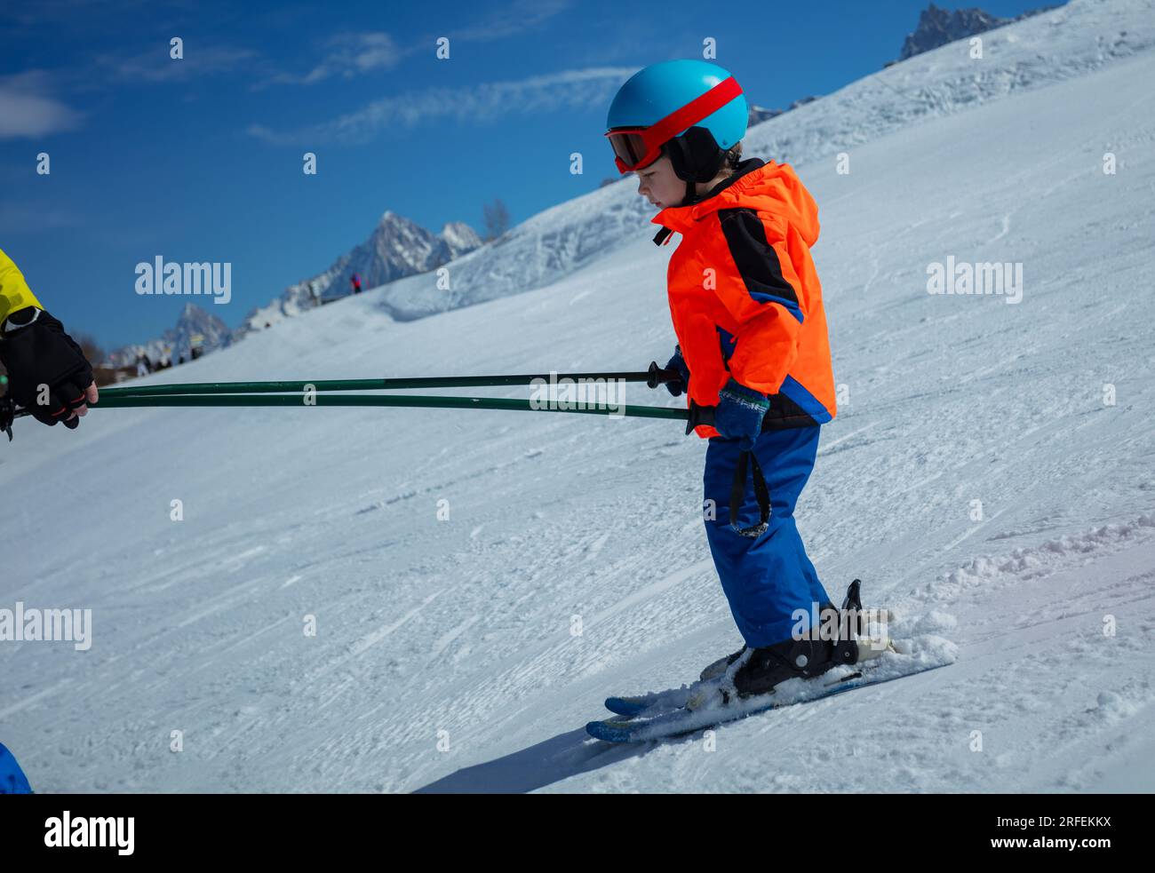 Profile view of child learn to ski with instructor holding poles Stock Photo