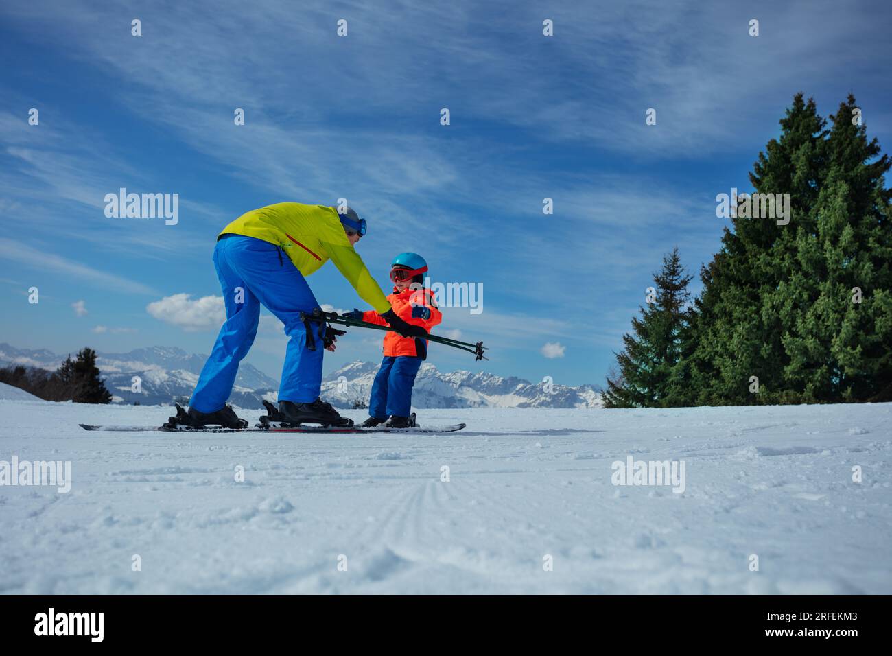 Dad show child how to ski going downhill holding poles in hands Stock Photo