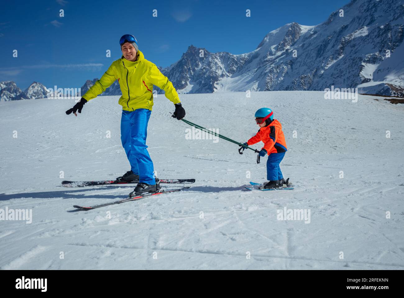 Instructor go downhill teach child to ski connected by poles Stock Photo